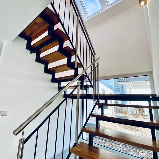 Moderne Holz-Metall-Treppe mit schwarzen Geländern und hellem Tageslicht durch Oberlichter