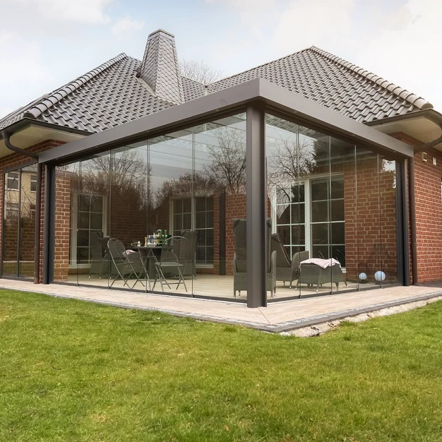 Moderne Verglasung als Wintergarten an ein Ziegelhaus mit Gartenmöbeln und Rasen vor dem Haus