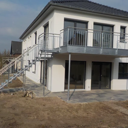 Weißes modernes Haus mit Balkonen und Treppe aufgenommen auf dem Baustellengrund
