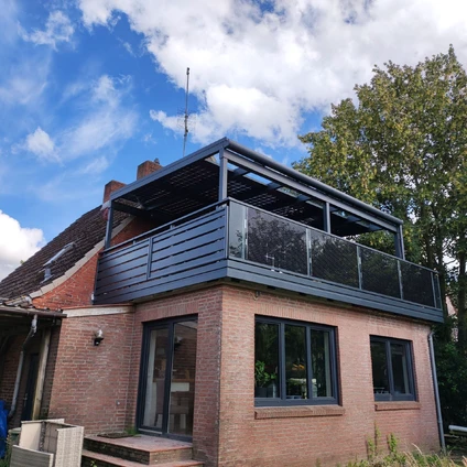 Backsteinhaus mit modernem Metallbalkon blauem Himmel und grünen Bäumen im Hintergrund