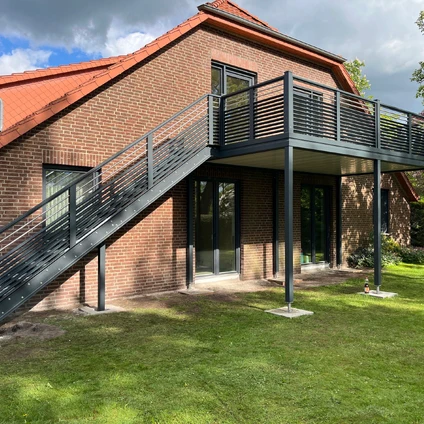 Modernes Backsteinhaus mit rotem Dach externem Balkon und Treppenaufgang auf grünem Rasen