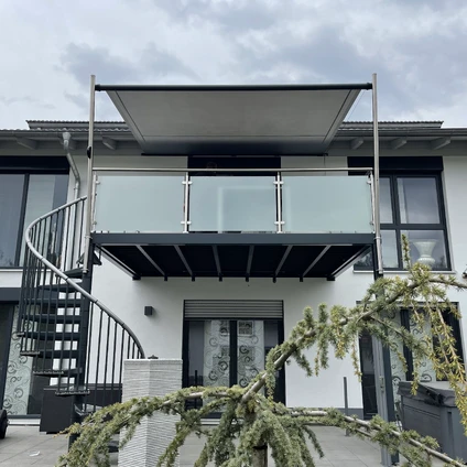 Moderne Fassade mit Balkon schwarzer Wendeltreppe und großen Glasfenstern vor Zweigen