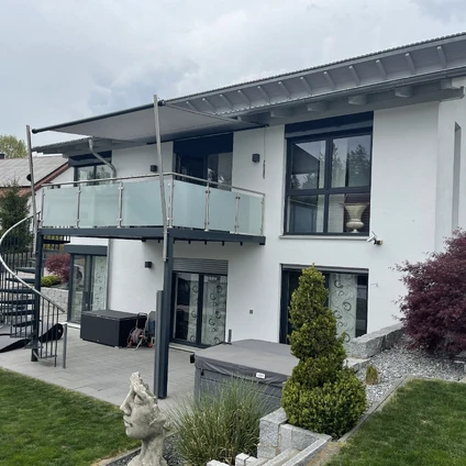 Modernes Haus in Weiß mit Balkon schwarzen Fenstern und grüner Gartenkulisse