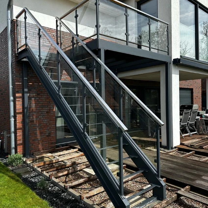 Industrielle Metalltreppe mit Glasgeländer an einer modernen Fassade neben Schienen