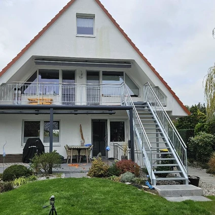 Modernes Haus mit weißem Dach externer Treppe und grünem Gartenvorplatz